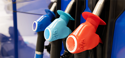 Close-up of Mobil fuel nozzles, showing two blue nozzles labeled E10 and a red nozzle labeled Supreme+. Each nozzle has a textured grip and a Mobil-branded label, indicating different fuel types.