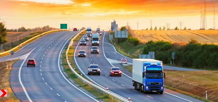Dual-carriage highway with medium traffic coming and just one car heading away. The sky is a bright evening orange