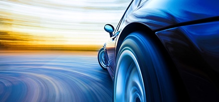Close-up view of a car wheel in motion on an open road, with a blurred effect suggesting high speed. The background features streaked colors of the landscape, blending into the road.